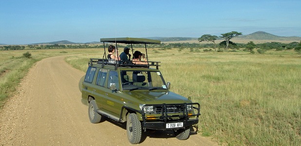 Två safariresenärer och deras guide spanar från takluckan på sitt fordon.
